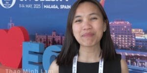 A woman wearing a black top and a lanyard stands in front of a conference backdrop displaying "Malaga, Spain" and event dates. Text on image reads "Thao Minh Lam, Netherlands.